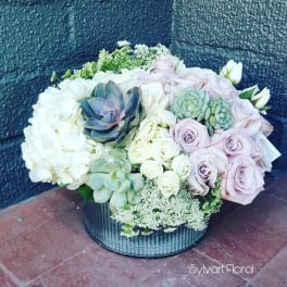 Round floral arrangement with pale roses, hydrangeas, and succulents in a black container