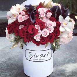 Red and pink roses with white orchids in a white hat box