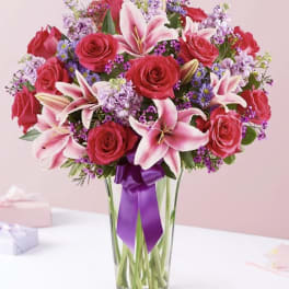 Pink roses and lilies arranged in a clear glass vase with a purple ribbon
