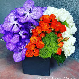 Purple orchids, orange roses, and white hydrangeas in a black square vase