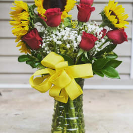 Bouquet of red roses and yellow sunflowers in a glass vase with a yellow ribbon