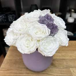 White roses arranged in a lavender vase with a purple crystal cluster