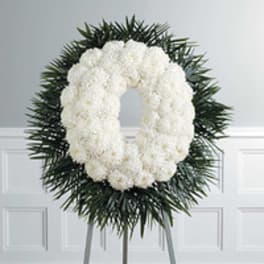 White floral funeral wreath on a stand with dark greenery