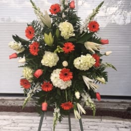 Standing floral spray with red gerberas, white lilies, and pale hydrangeas