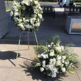 White floral funeral wreath on an easel beside a matching floor spray