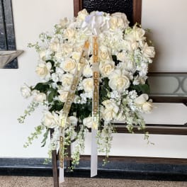 Large white rose funeral spray with ribbon streamers on a stand