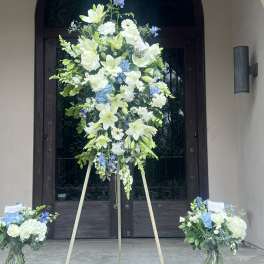 Large standing floral spray with white and blue flowers on a tripod easel