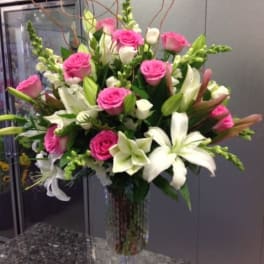 Pink roses and white lilies arranged in a tall glass vase