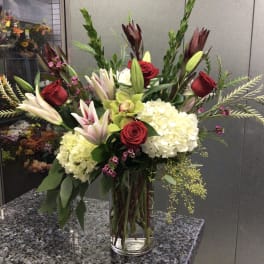 Tall bouquet of red roses, lilies, and white hydrangeas in a glass vase