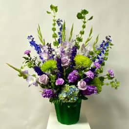 Tall mixed bouquet of purple, blue, and green flowers in a green container