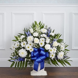 White daisies and roses arranged in a white vase with a blue ribbon