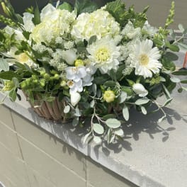 White floral arrangement in a woven basket with mixed greenery