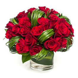 Red rose bouquet in a clear glass vase with folded green leaves