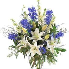 White lilies and blue flowers in a clear glass vase