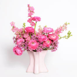 Pink ranunculus and small pink blossoms in a pale vase