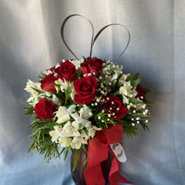 Red roses and white flowers in a dark vase with a red ribbon