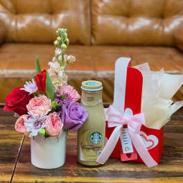 Small flower arrangement with a gift bottle and wrapped box on a table