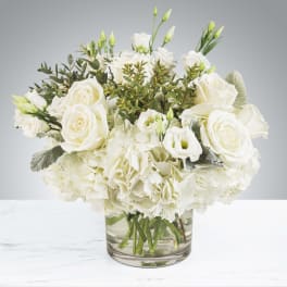 Low round arrangement of white roses, lisianthus, and hydrangeas in a clear glass vase