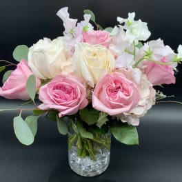 Compact arrangement of pink and cream roses with soft blush blooms in a clear glass vase.