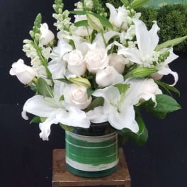 White lilies and pale roses arranged in a green glass vase