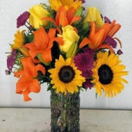 Bouquet of sunflowers, orange lilies, and purple flowers in a glass vase