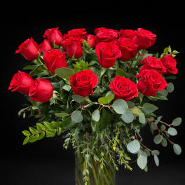 Red roses arranged in a clear glass vase with eucalyptus