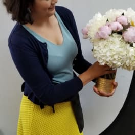 Woman holding a white and pale pink flower arrangement in a gold vase
