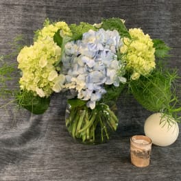 Hydrangea arrangement in a glass vase with a candle and white orb