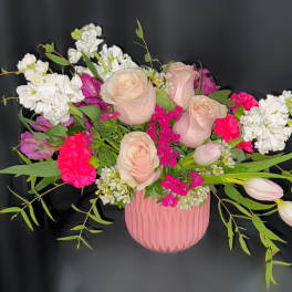 Pink and white roses arranged in a pink vase with greenery