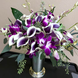 Purple and white calla lilies with orchids in a black vase