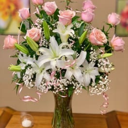 Pink roses and white lilies in a glass vase with pink ribbon curls