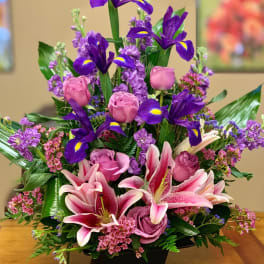 Pink roses and lilies arranged with purple irises in a black vase