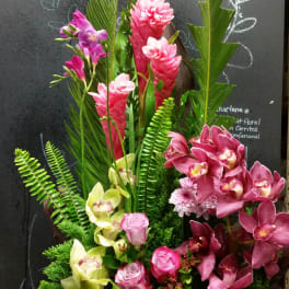Tall tropical bouquet with pink orchids and green foliage in a black container