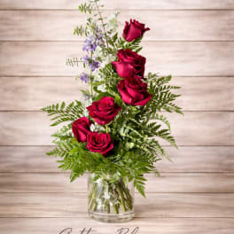 Red roses in a clear glass vase with mixed greenery and small purple flowers
