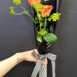 Two orange roses wrapped in black paper with a striped ribbon