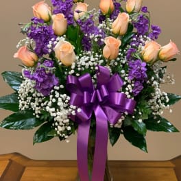 Bouquet of peach roses and purple flowers in a glass vase with a purple ribbon
