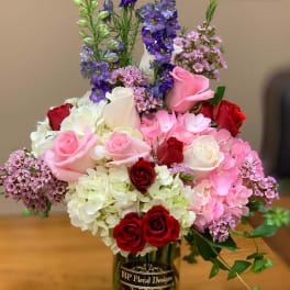 Mixed bouquet of roses, hydrangeas, and purple flowers in a glass vase