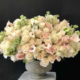 Large bouquet of cream and blush roses with calla lilies in a stone vase