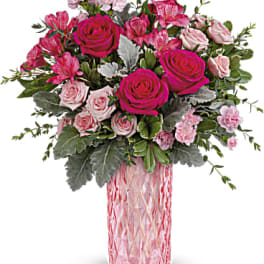 Pink and hot pink roses, alstroemeria, and carnations in a tall textured pink glass vase.