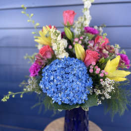 Colorful mixed bouquet in a blue glass vase with hydrangea, lilies, and roses