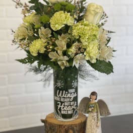 Cream and green floral arrangement in a decorated glass vase beside a small angel figurine.