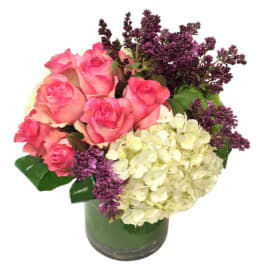 Bouquet of pink roses, white hydrangeas, and purple lilacs in a glass vase with green wrap