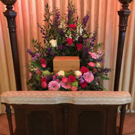 Large funeral floral arrangement with roses and daisies around a wooden urn