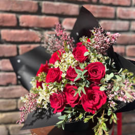 Bouquet of red roses with small white filler flowers in black wrap