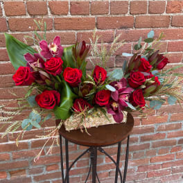 Red roses and burgundy orchids in a low rectangular arrangement