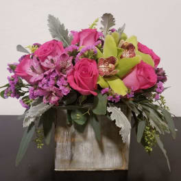 Pink roses and orchids in a square vase with silver foliage