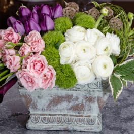 Arrangement of pink, purple, and white flowers in a weathered rectangular planter