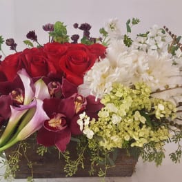 Mixed floral arrangement with red roses, white blooms, and burgundy orchids in a wooden box