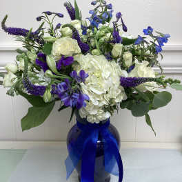 White and blue floral arrangement in a dark vase with a blue ribbon