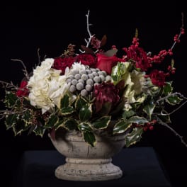 Red and white floral arrangement in a stone urn with berries and branches